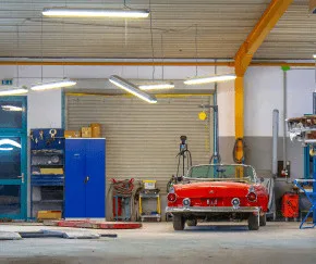 Une voiture décapotable rouge est garée dans un garage avec des étagères, des outils et des équipements visibles autour d'elle.